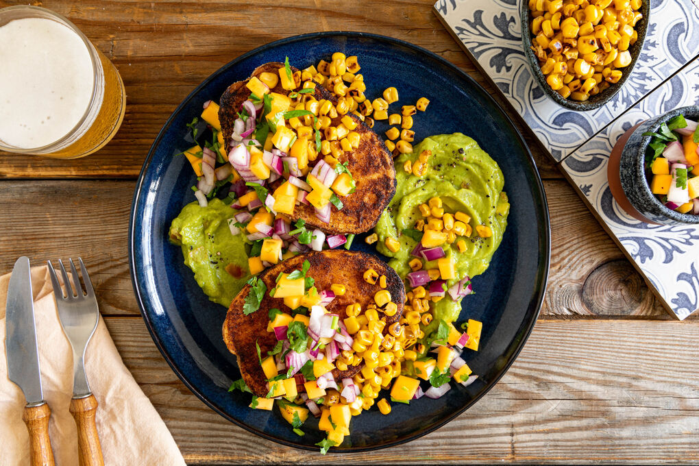 Mexikanische Kumpir mit Kaki-Salsa und geröstetem Mais, serviert auf Guacamole