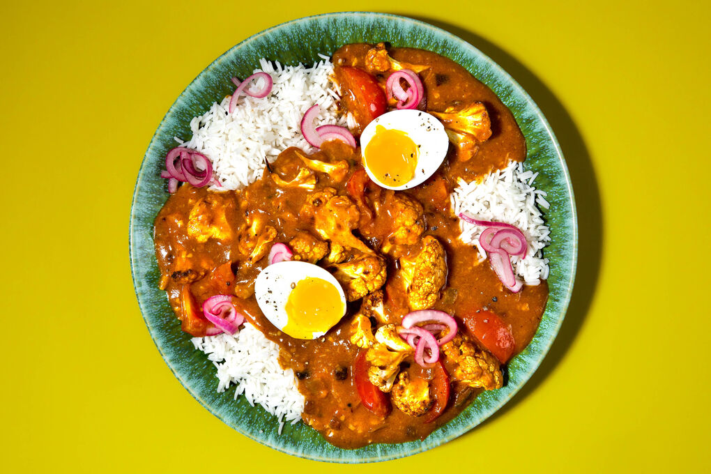 Blumenkohl-Curry mit weichem Ei auf Reis, serviert mit eingelegten Zwiebeln