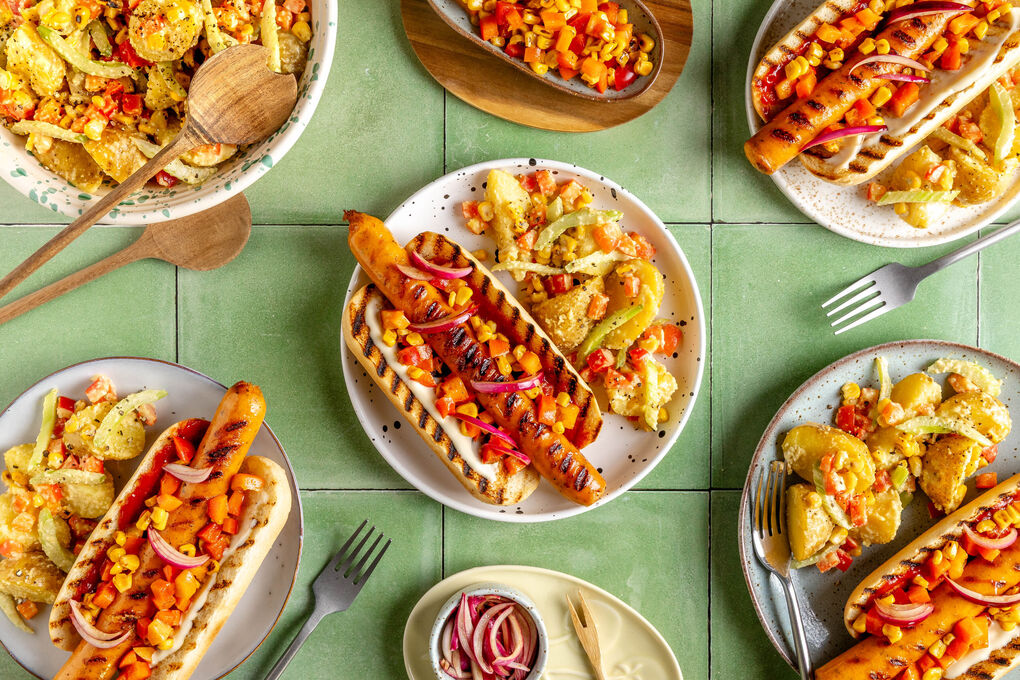 Hotdog mit Geflügelwurst und Mais-Salsa dazu Kartoffel-Erdnuss-Salat