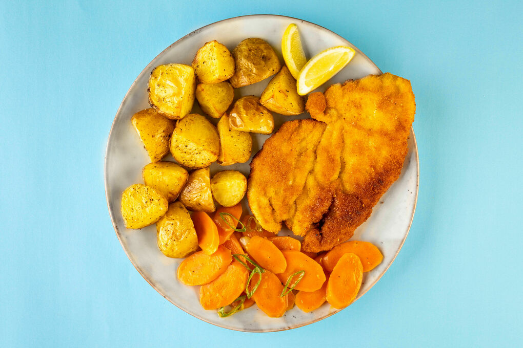 Knuspriges Hähnchenschnitzel dazu Röstkartoffeln, Karotten und Zitrone