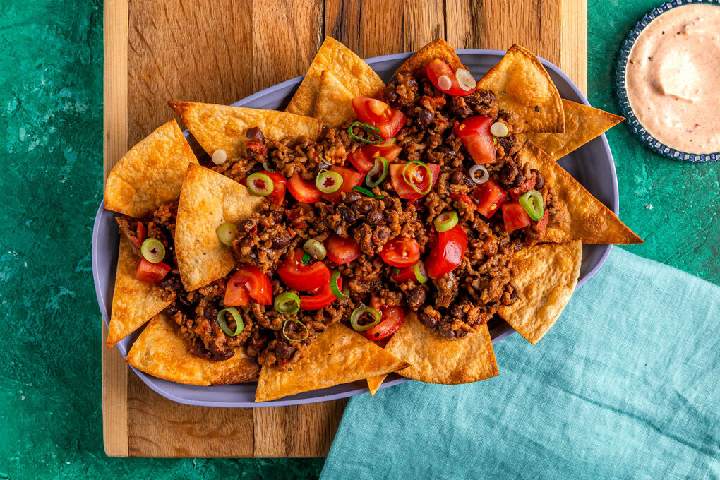 Loaded Nachos mit Chili con Carne garniert mit Lauchzwiebeln und Tomaten