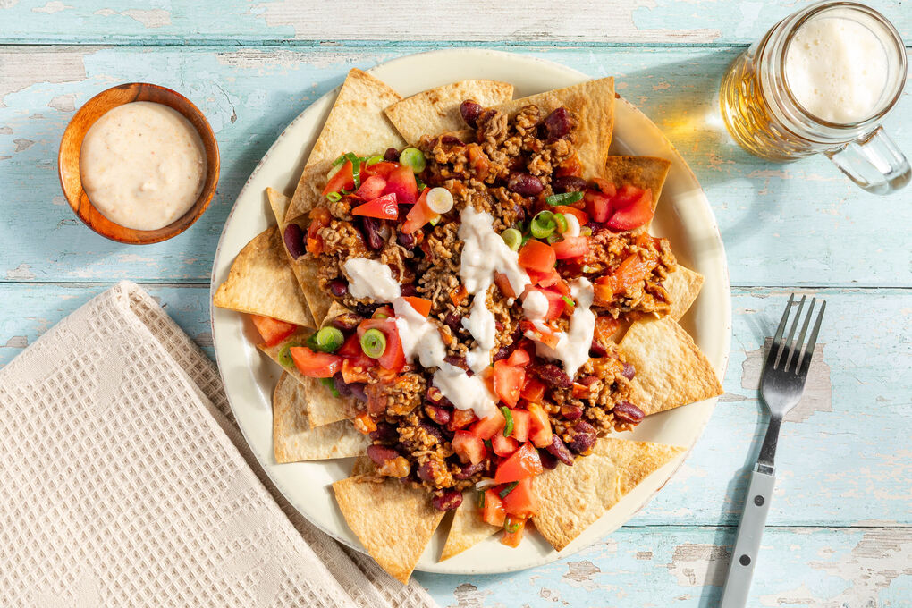 Loaded Nachos mit Chili con Carne garniert mit Lauchzwiebeln und Tomaten