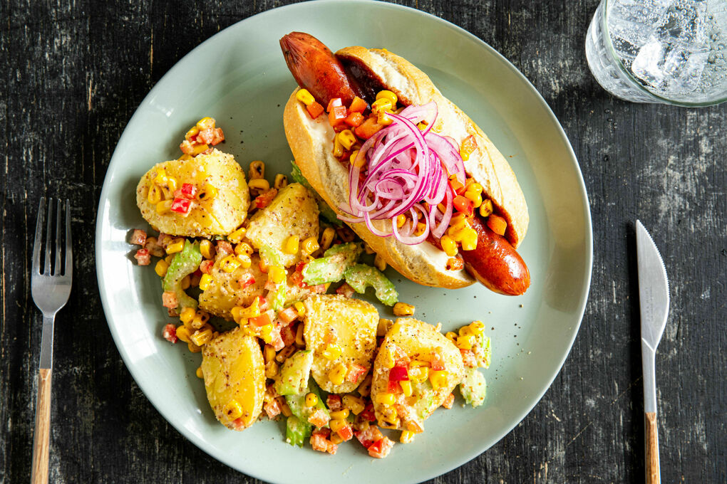 Hotdog mit Geflügelwurst und Mais-Salsa dazu Kartoffel-Erdnuss-Salat